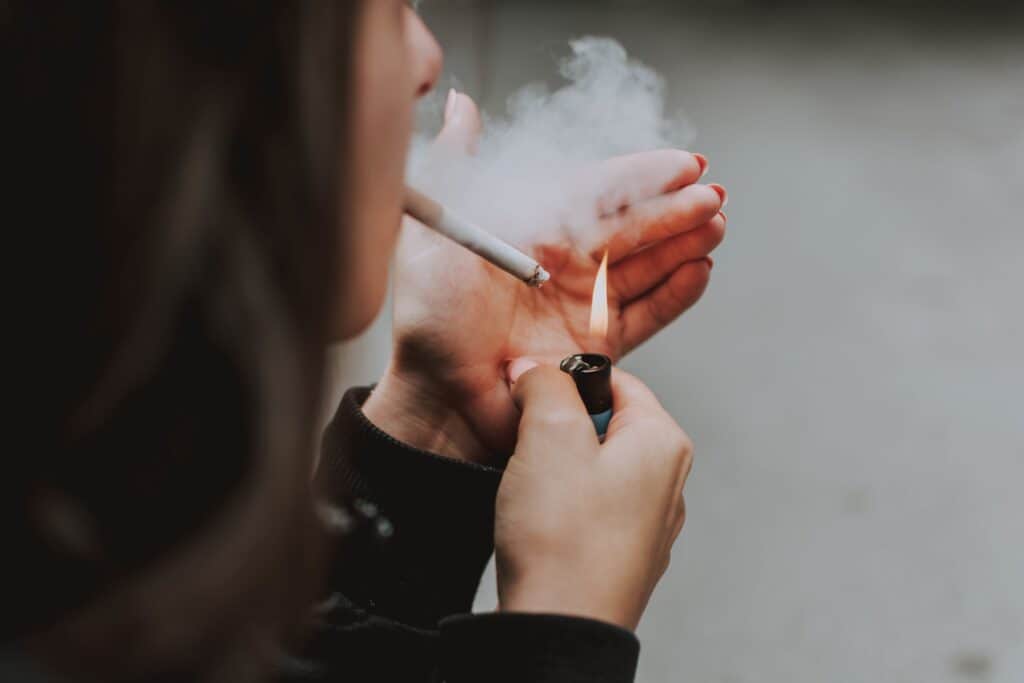 A woman is lightning up cigarette with lighter